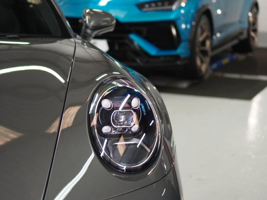 Freshly protected Porsche headlight and bonnet, with a wrapped Lamborghini Urus in the background